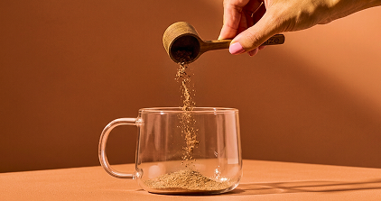 Hand pouring tea into a glass mug with a brown background