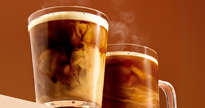 Two steaming mugs of hot liquid against a brown background