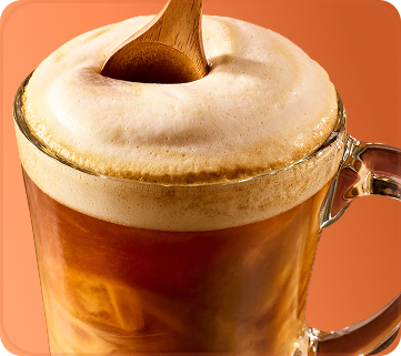 Glass mug with a creamy top and wooden spoon on an orange background