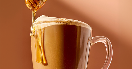 Honey being drizzled into a cup of coffee on a brown background