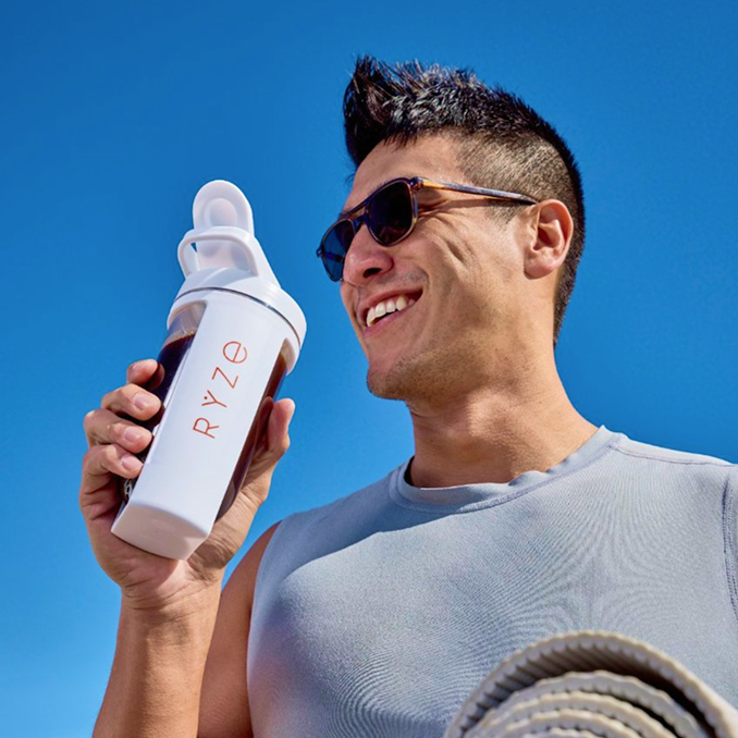 Man holding a RYZE water bottle against a clear blue sky